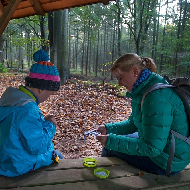 Mutter und Kind sitzen im Wald in einer Schutzhütte mit einem Geocache
