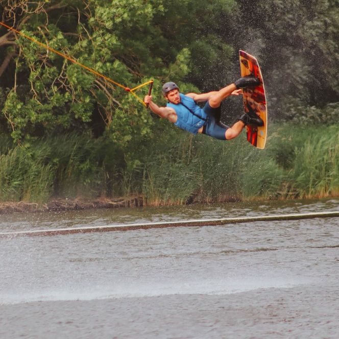 Ein Wakeboarder beim Stunt in der Luft auf dem Board hält sich mit einer Hand am Seil fest