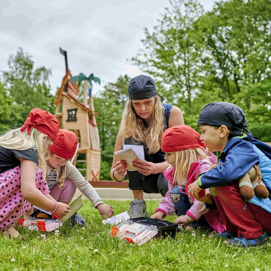 Mutter mit Kindern beim Escapegame, versammelt um die Ausrüstung auf einer Wiese 