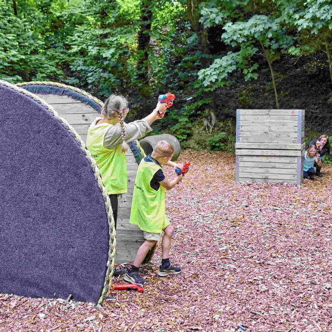 Mutter und Kind verstecken sich in einer Kabeltrommel und zielen auf eine Holzwand in der Nerfarena Wingst