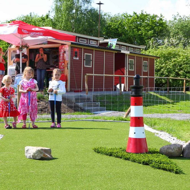 Adventuregolfanlage mit Kindern in Neuhaus mit Green und im Hintergrund ein Holzhaus