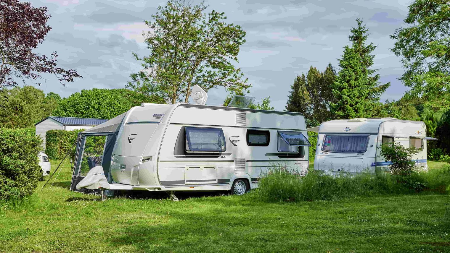 Zwei Wohnwagen auf einer Campingwiese mit Bäumen
