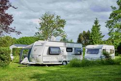 Zwei Wohnwagen auf einer Campingwiese mit Bäumen