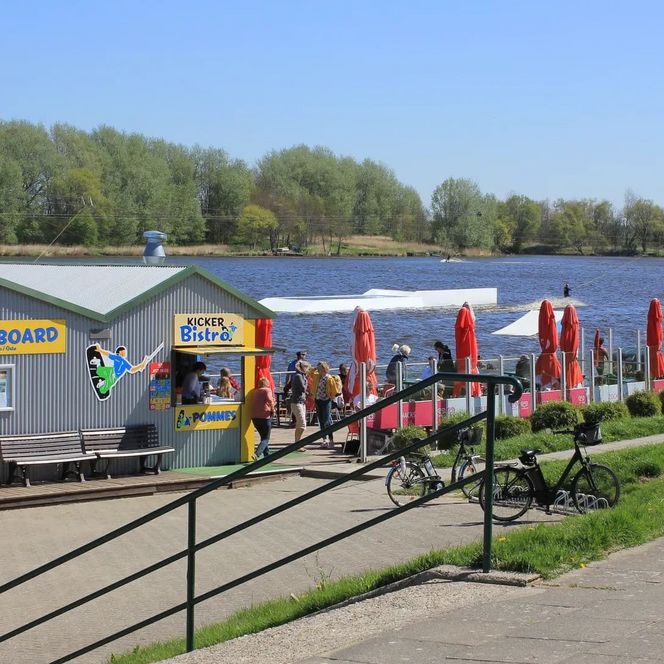 Sommerblick von der Zuwegung auf das Bistro der Wasserskianlage und den Treppenabgang. Im Hintergrund der Ostesee