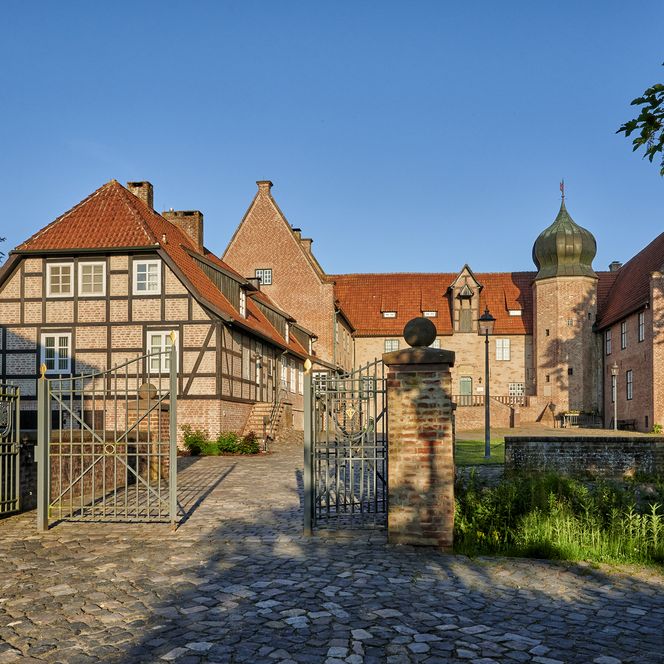 Die Burg Bederkesa wird an einem Sommertag unter blauem Himmel von der Sonne angestrahlt.