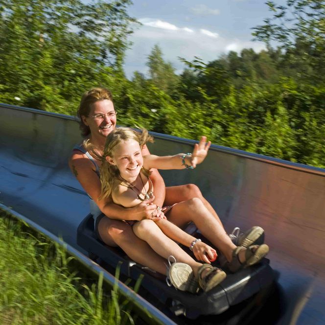 Mutter mit Tochter auf einen Schlitten der Sommerrodebahn in voller Abfahrt