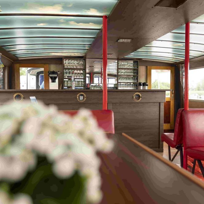 Innenansicht der Ausflugsschiff MS Mocambo mit rote gespolsterten Bänken. Im Hintergrund die Bordbar.