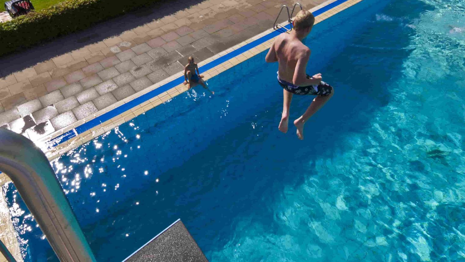 Sicht vom Sprungturm hinunter in das Becken, ein Junge springt gerade vom Turm ins Wasser